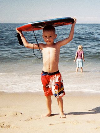 Smiling boy carrying a boogie board out of the ocean at Head of the Meadow Beach